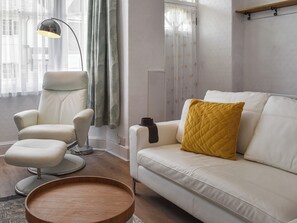 A modern living room with a white leather sofa, a round wooden coffee table, a high chair, and a floor lamp.