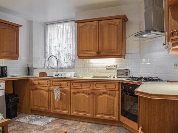 A kitchen with wooden cabinets, a gas stove, a microwave, and a sink.