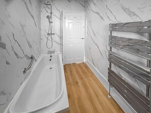 A bathroom with a white bathtub, a shower, and a wooden floor.