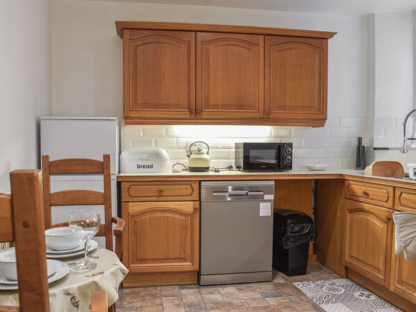 A kitchen with wooden cabinets, a refrigerator, a microwave, a bread maker, and a dishwasher.