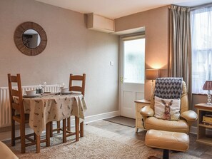 A dining area with a table set for two, a mirror on the wall, a sofa with a patterned pillow, and a window with curtains.