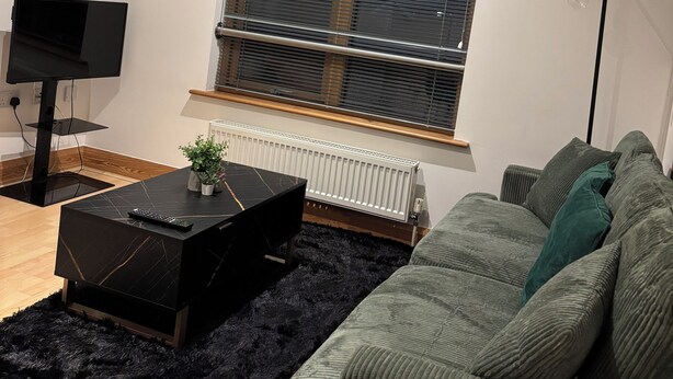 A living room with a TV, a clock, a radiator, and a sofa. - 1 bed apartment in Norwich city centre (Norwich)