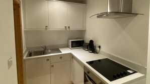 A compact kitchen with white cabinets, a microwave, a coffee maker, and a stove. - 1 bed apartment in Norwich city centre (Norwich)