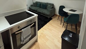 A compact living space with a kitchenette, a sofa, a small round table, and a trash bin. - 1 bed apartment in Norwich city centre (Norwich)