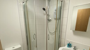 A bathroom with a glass-enclosed shower, a toilet, and a sink with a mirror above it. - 1 bed apartment in Norwich city centre (Norwich)
