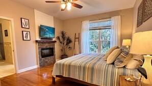 Ein Schlafzimmer mit einem großen Bett, einem Kamin, einem Deckenventilator und einem Fenster mit Vorhängen.