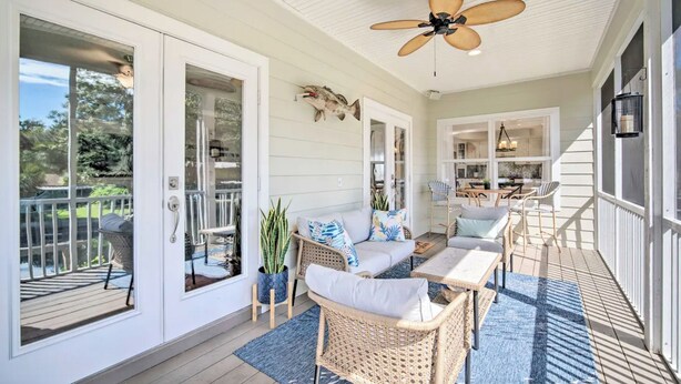 Eine überdachte Veranda mit Korbmöbeln, einem Deckenventilator und Blick auf den Garten.