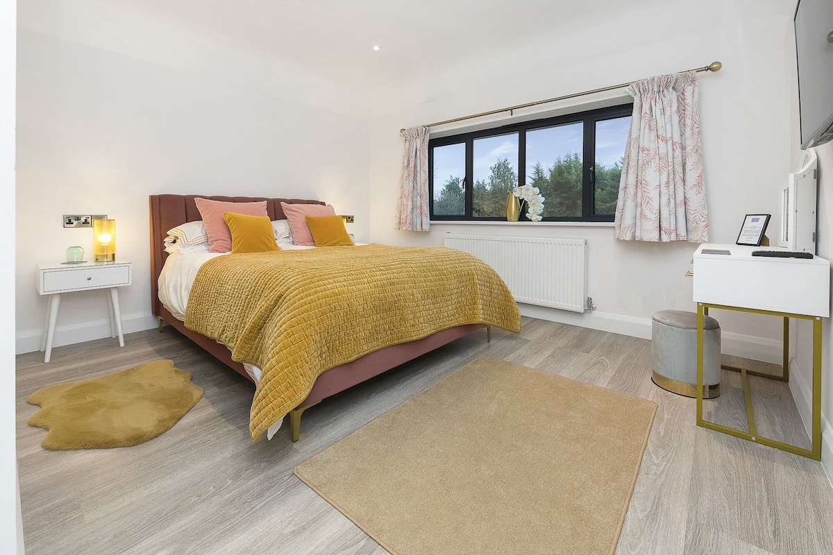 Quarto com cama, mesas de cabeceira, escrivaninha, janela com cortinas e radiador.