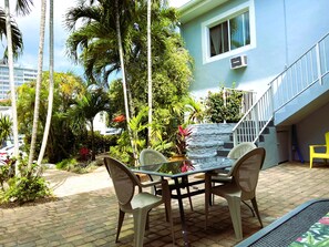 An outdoor patio with a table and chairs, surrounded by lush greenery and a staircase leading to a building. - Beach Tide (Hollywood)