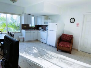 A compact kitchen with white appliances, a dining area with a table and chairs, and a red patterned chair. - Beach Tide (Hollywood)