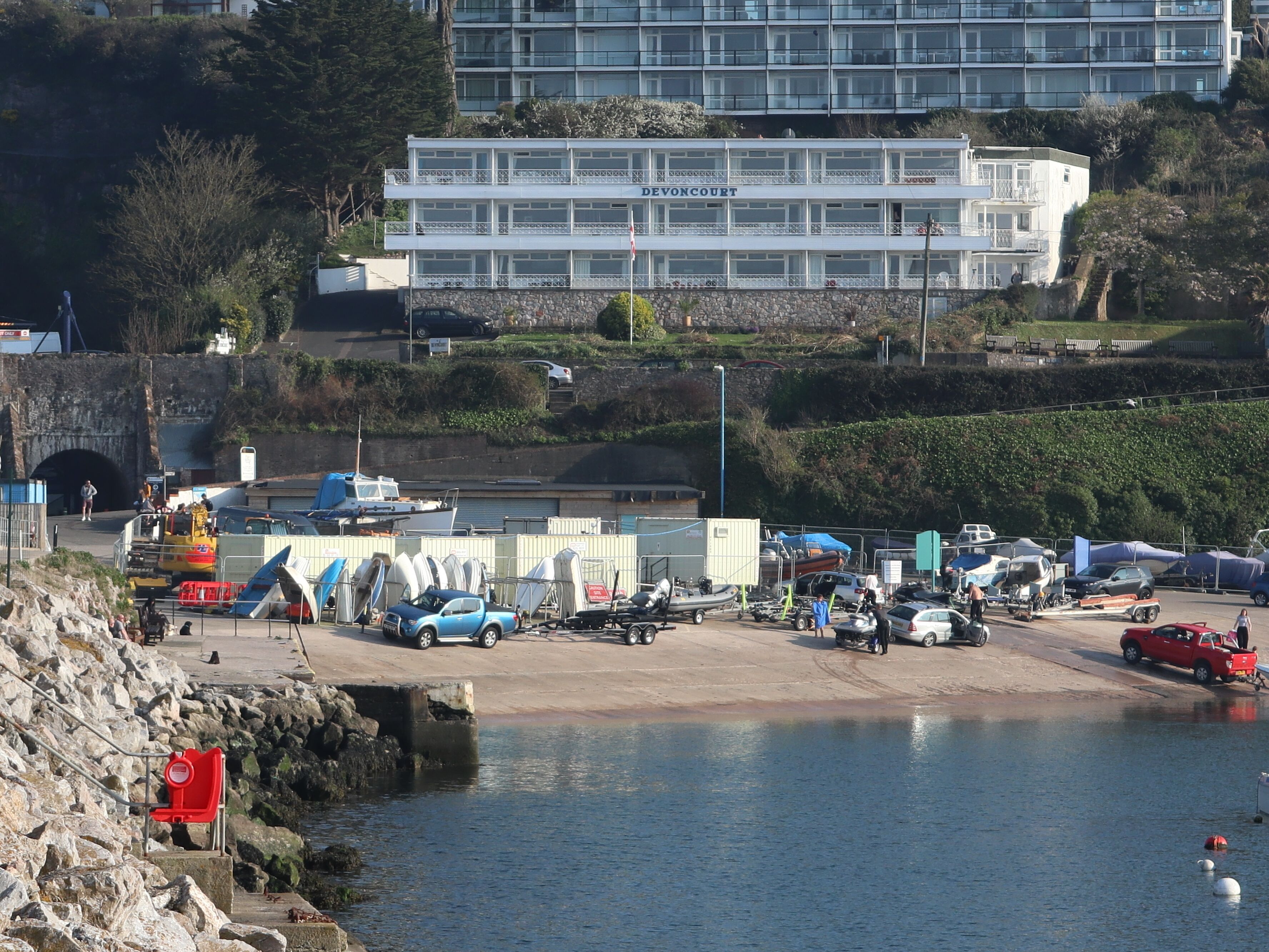 Una zona costera con un puerto deportivo, barcos y un edificio de varios pisos con la inscripción "DEVONCOURT".