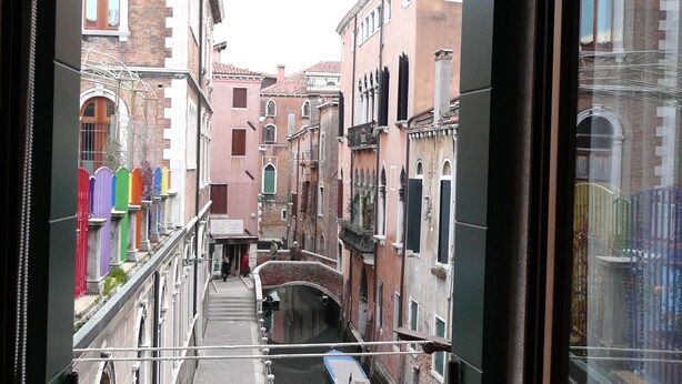 A narrow canal with boats, flanked by historic buildings with arched windows and brick facades.