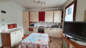 A compact kitchen with a dining table, microwave, stove, sink, and a flat-screen TV.