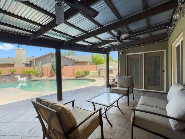 Un patio couvert avec une piscine, du mobilier d’extérieur et une vue sur le jardin arrière.