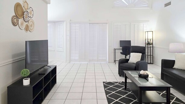 A modern living room with a flat-screen TV, black furniture, a ceiling fan, and a large window with blinds. - Wow! 3BDR Single-story home in Tempe/Chandler (Tempe)
