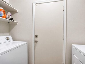 Una sala de lavandería con una lavadora blanca, una secadora y un estante con productos de limpieza.