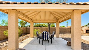 A covered patio with a table and chairs, surrounded by a brick wall and vegetation. - Pet-Friendly 3BR | King Bed | Fenced Yard (Tempe)