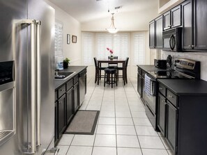 A modern kitchen with stainless steel appliances, dark cabinetry, and a dining area with a table and chairs.