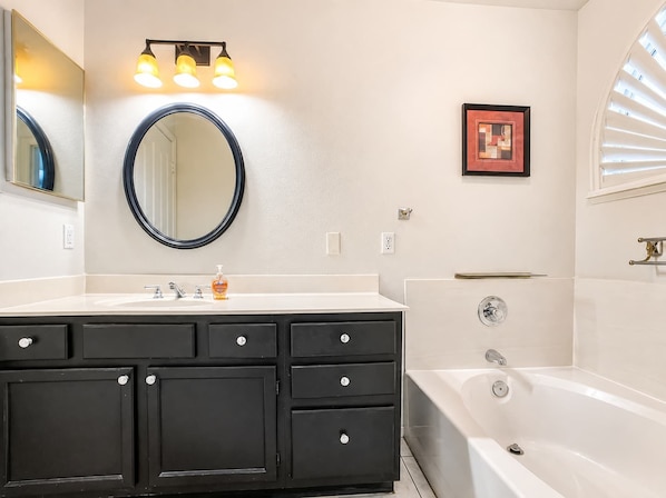 Un baño con lavamanos blanco, tocador negro, espejo redondo y bañera.
