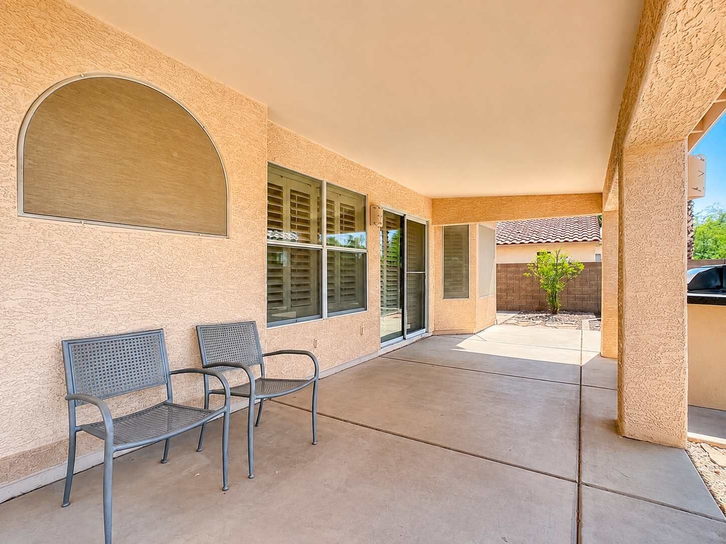 Un patio cubierto con dos sillas de metal, piso de concreto y vista de un edificio residencial al fondo.