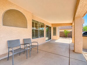 Un patio cubierto con dos sillas de metal, piso de concreto y vista de un edificio residencial al fondo.