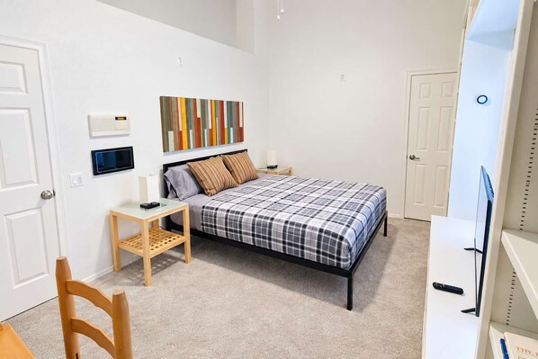 A bedroom with a bed, bedside tables, a chair, a TV, and a wall-mounted artwork.