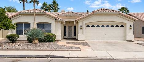 A two-story house with a garage, palm trees, and a clear sky.