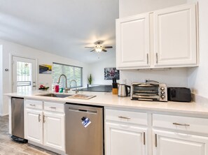 A modern kitchen with white cabinetry, a stainless steel dishwasher, a built-in oven, a toaster, and a coffee maker.