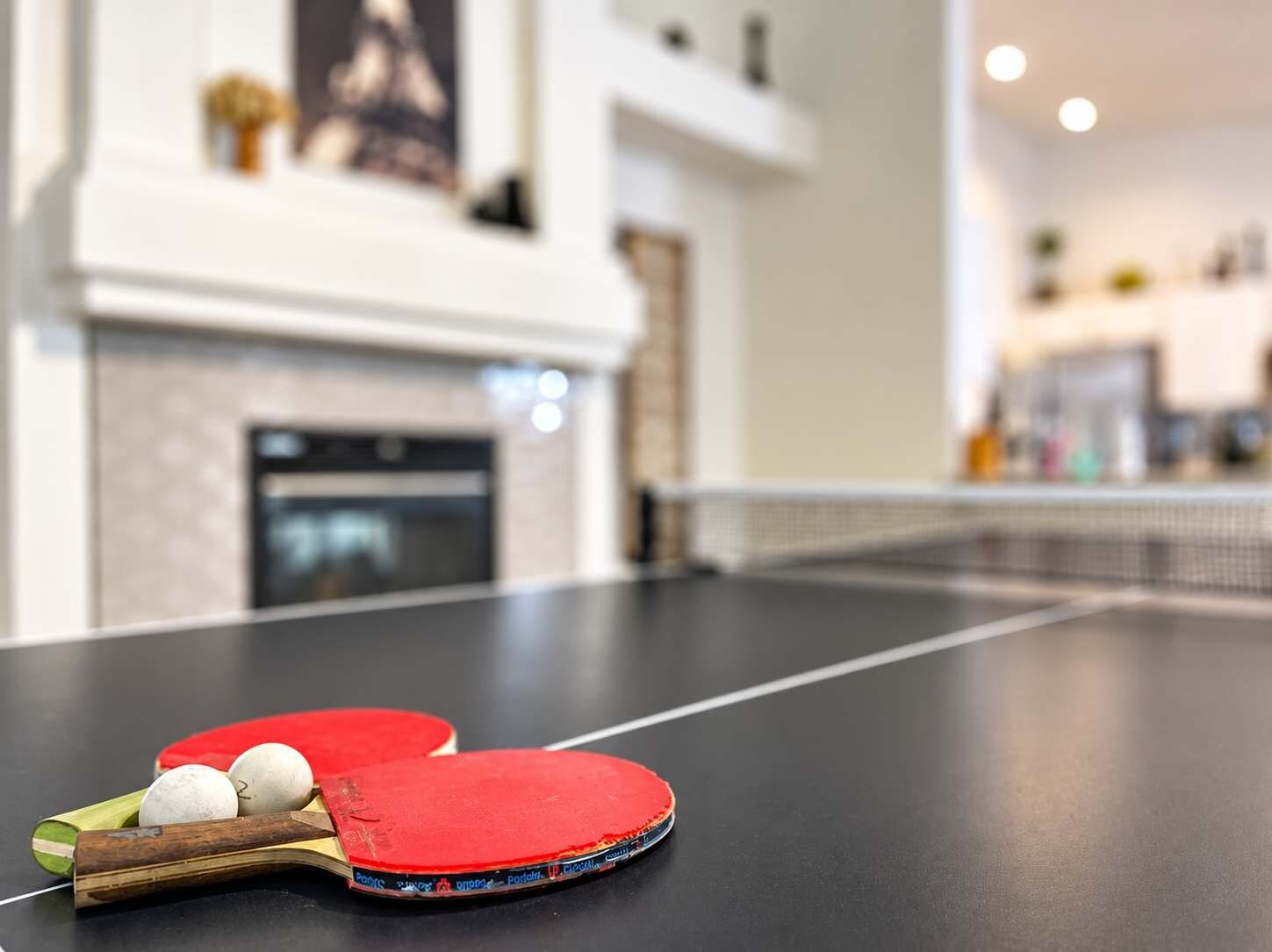 A ping pong table with paddles and balls, a fireplace, and a modern interior.