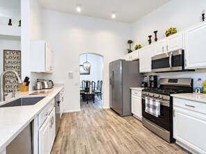 A modern kitchen with white cabinetry, stainless steel appliances, and a wooden floor. - Nice! 5 Bedroom Single-Story Chandler Home (Chandler)