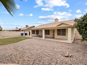 A residential building with a covered patio, a gravel driveway, and a clear sky.