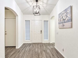 A hallway with a wooden floor, white walls, a door with a window, and a ceiling light fixture.