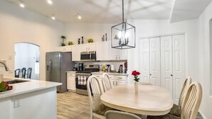 Une cuisine moderne avec des meubles blancs, un îlot central et un coin repas comprenant une table ronde et des chaises.