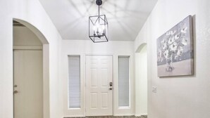 Un couloir avec un plancher en bois, des murs blancs, une porte et un luminaire au plafond.