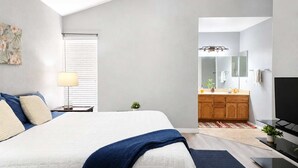 Une chambre à coucher avec un lit, une table de chevet, une lampe et une vue sur la salle de bain.