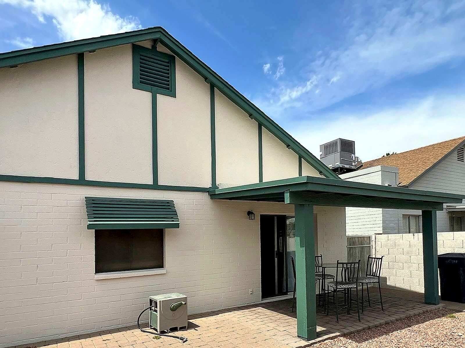 A building with a covered patio area, a brick wall, and a window with blinds.