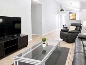 A modern living room with a flat-screen TV, a glass-top coffee table, a leather sofa, and a black leather chair. - Pet-Friendly 3BR | Fenced Yard | King Bed (Chandler)
