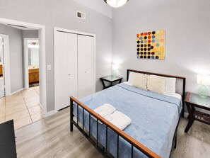 A hotel room with a bed, bedside tables, a bathroom with a mirror, and a wall art piece. - Pet-Friendly 3BR | Fenced Yard | King Bed (Chandler)