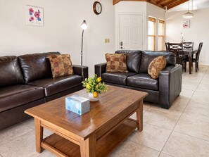 A living room with two leather sofas, a wooden coffee table, and a dining area with a table and chairs.