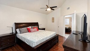 A bedroom with a bed, nightstands, a dresser, a ceiling fan, and a television.