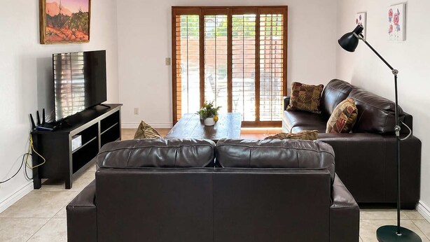 A living room with a dark leather sofa, a TV, a coffee table, and a floor lamp.