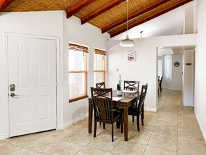 A dining area with a wooden table and chairs, a white door, and a ceiling with exposed beams.