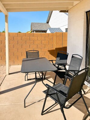 Un patio al aire libre con una mesa y cuatro sillas, un muro de ladrillo y un edificio al fondo.