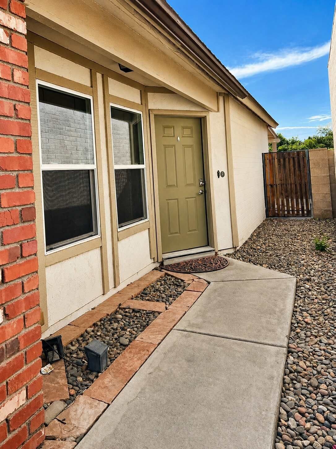 A residential building with a front door, two windows, a brick wall, and a gravel pathway.