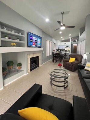 A modern living room with a fireplace, a television, and a dining area in the background. - Pet-Friendly 3BR | Private Pool | Game Room (Chandler)