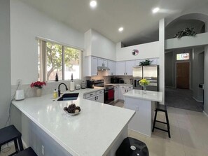 A modern kitchen with white cabinetry, a large island, and a view of the outdoors. - Pet-Friendly 3BR | Private Pool | Game Room (Chandler)