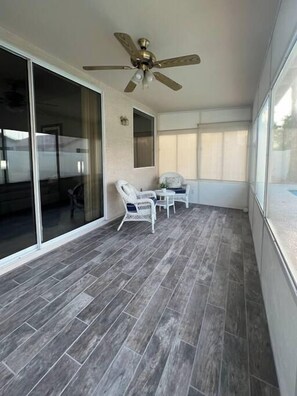 A balcony with grey tiled flooring, white wicker chairs, a ceiling fan, and a sliding glass door.