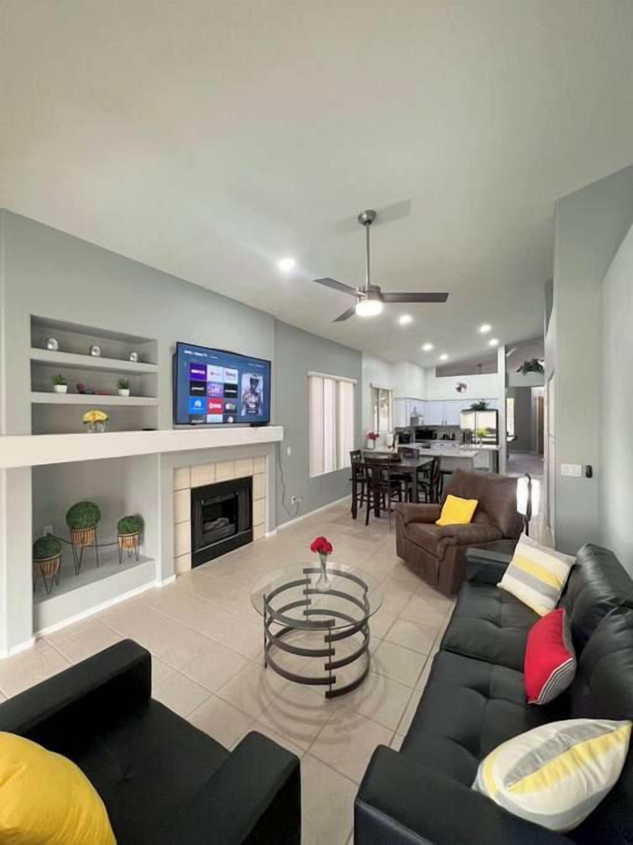 A modern living room with a fireplace, a dining area, and a kitchen in the background.