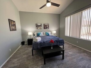 A bedroom with a bed, two bedside tables, a ceiling fan, and a large window with blinds. - Pet-Friendly 3BR | Private Pool | Game Room (Chandler)