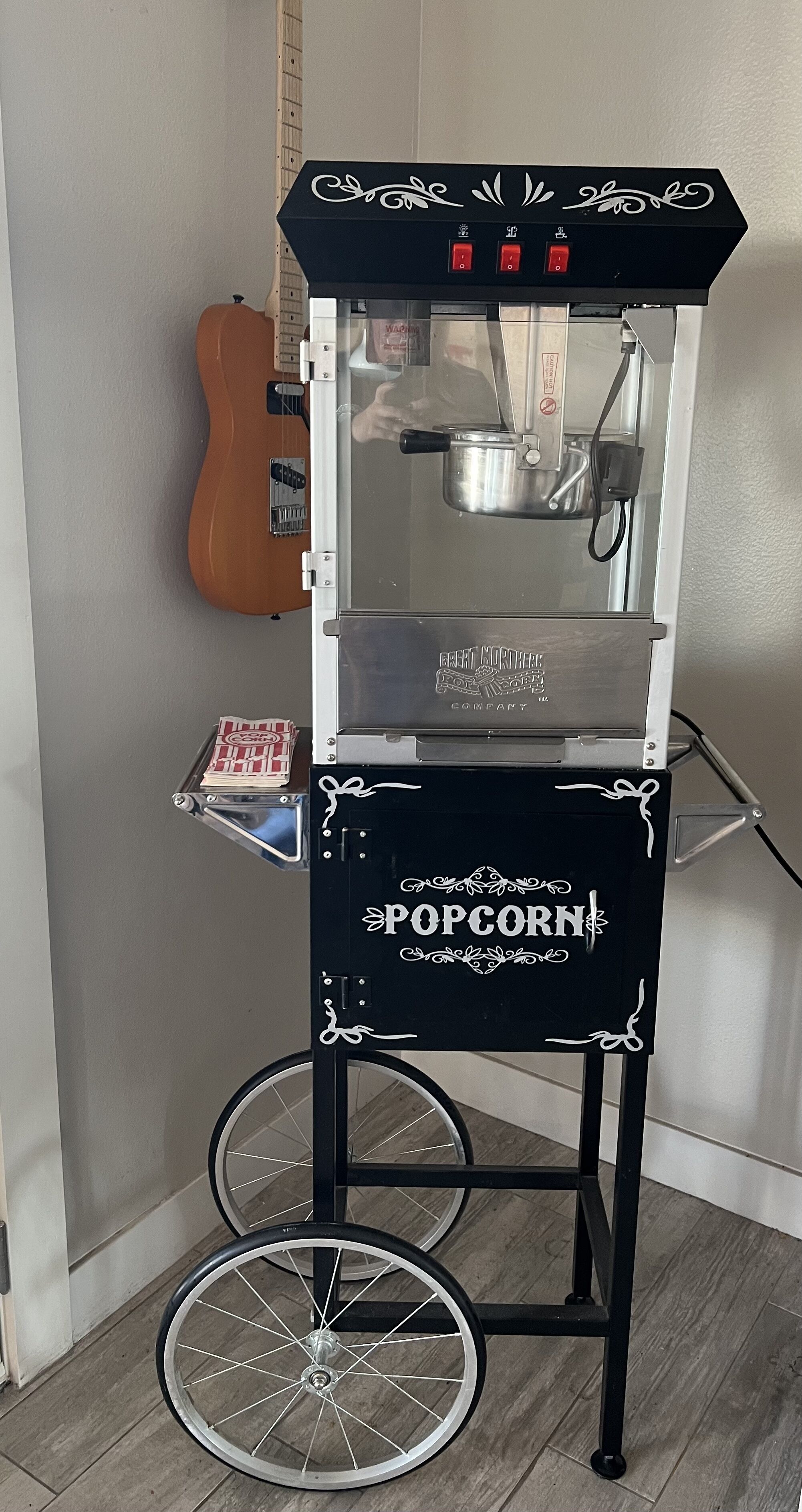 A popcorn cart with a clear glass enclosure, a metal pot inside, and a sign that reads 'POP CORN'.